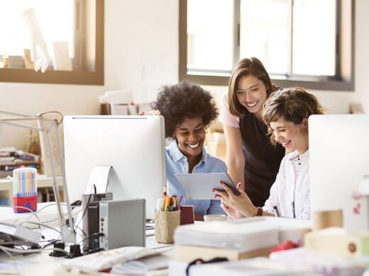 Happy multi-ethnic businesswomen using digital tablet at desk in office