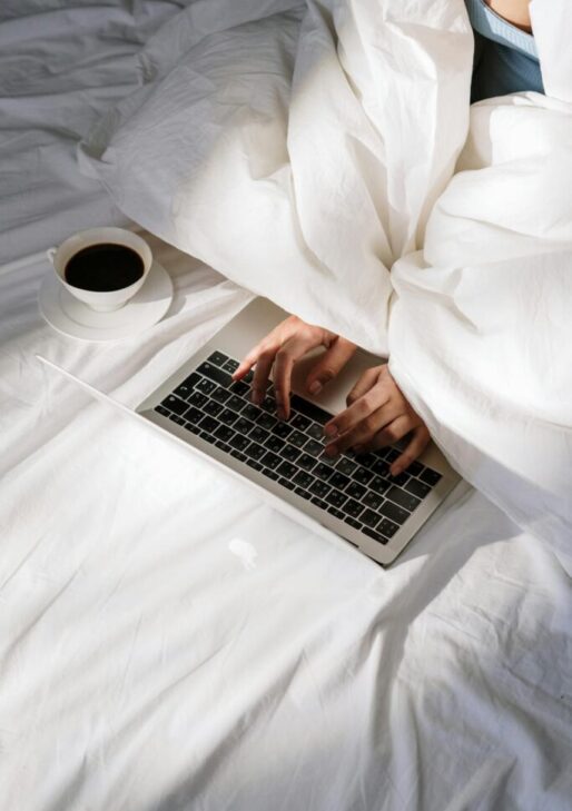 Person typing on a laptop in bed with a cup of coffee nearby, next to text outlining the steps: Book a Call, Have a Conversation, and Get a Proposal.